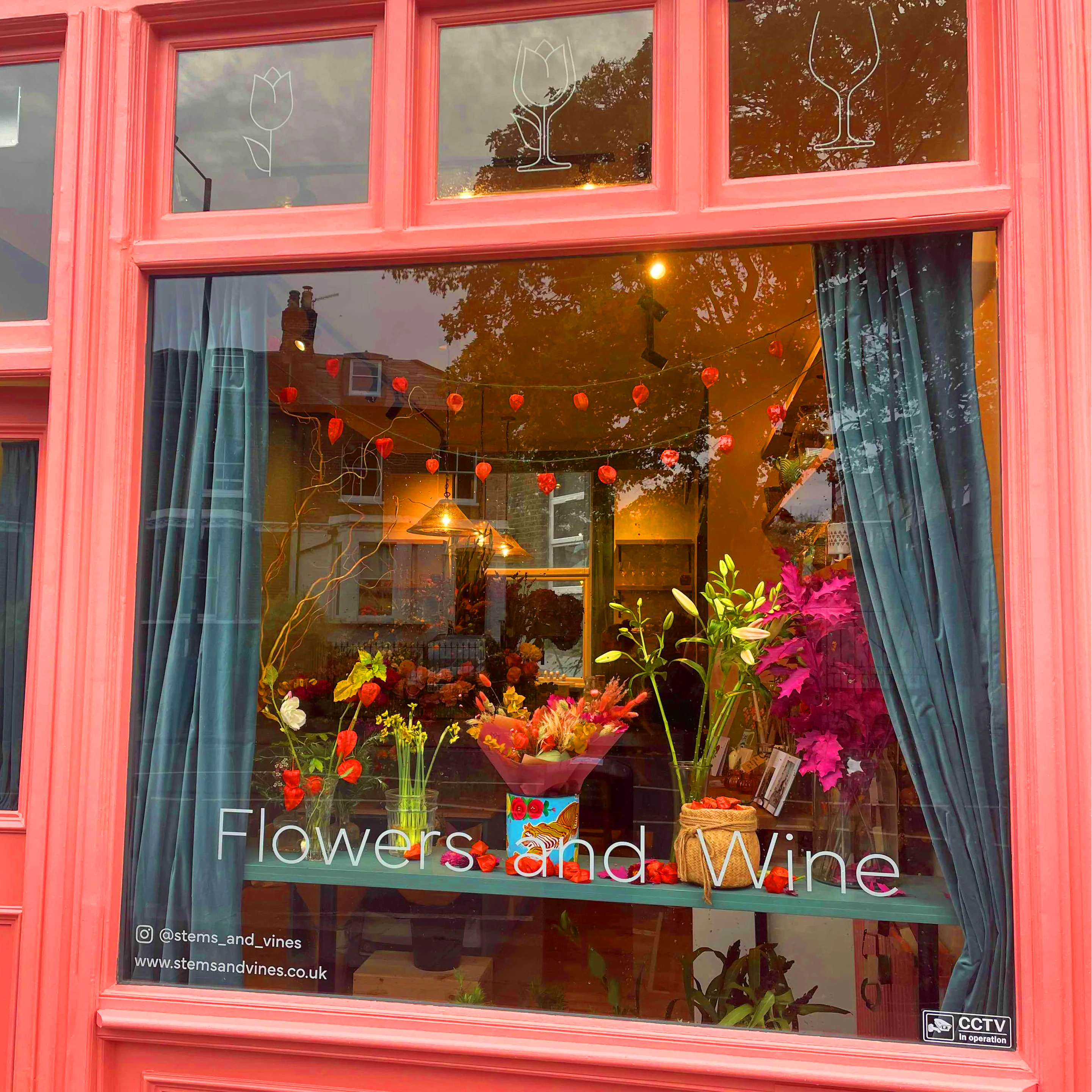 Pink door with glass panels displaying flowers and wine bottles, with 'Flowers and Wine' text.